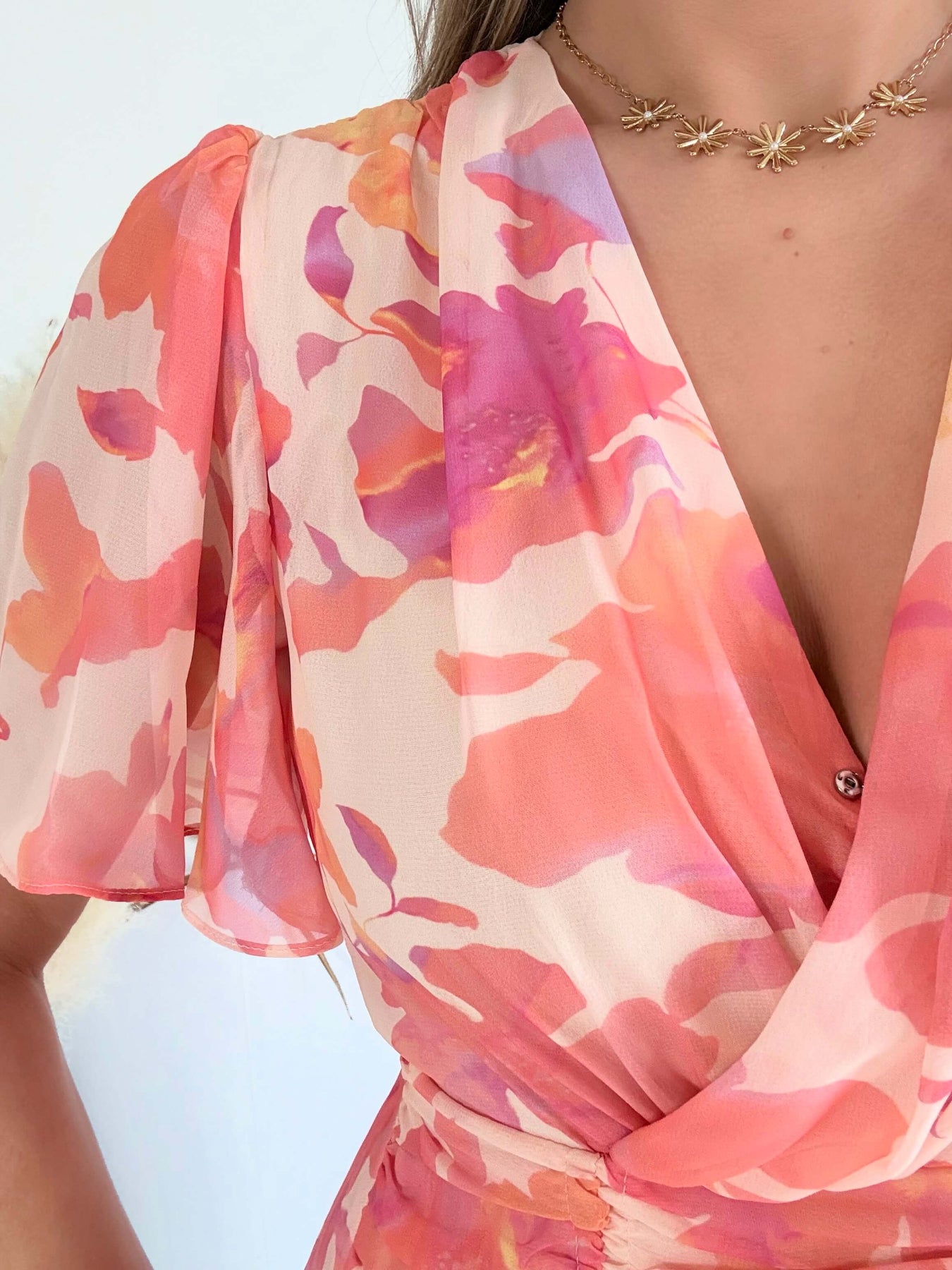 Robe courte rose et pêche imprimée Maëlia avec manches fluides, décolleté cache-cœur et jupe volantée portée par une femme.
