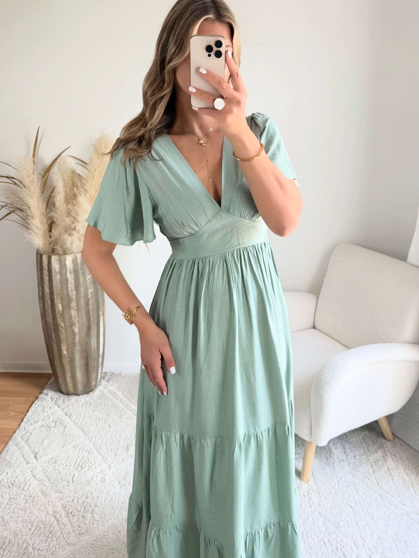 Femme portant une robe longue vert sauge fluide avec manches courtes et décolleté cache-cœur, style bohème chic.