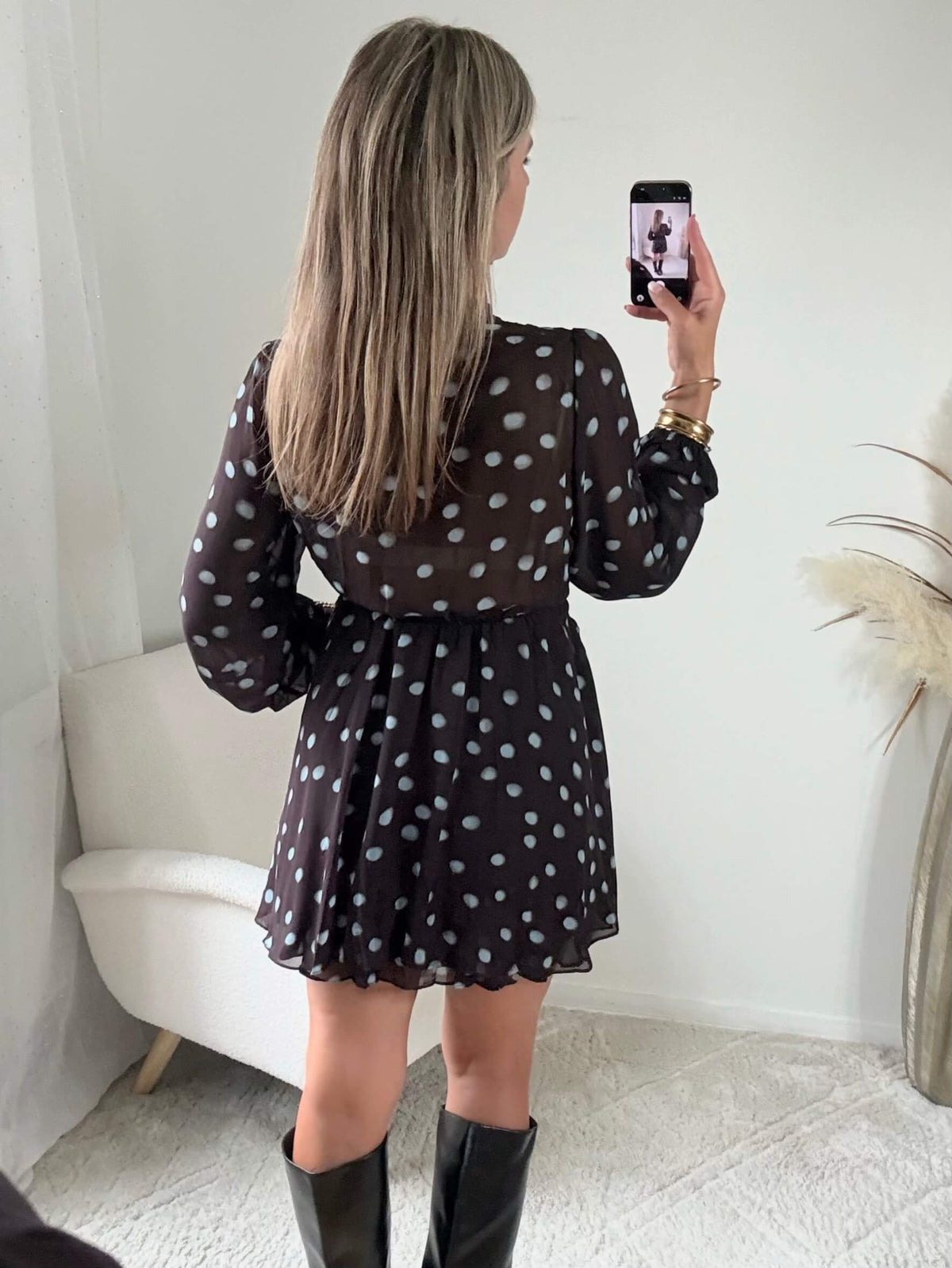 Robe courte marron Nae à pois bleu ciel, du S au L, avec décolleté cache-cœur, manches longues et jupe à volants, portée avec des bottes noires.
