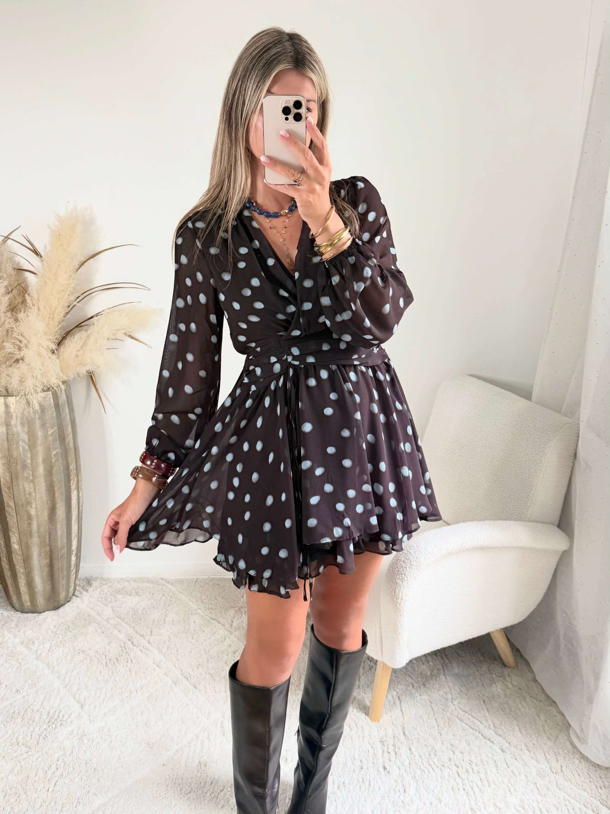 Robe courte marron Nae à pois bleu ciel, du S au L, avec décolleté cache-cœur, manches longues et jupe à volants, portée avec des bottes noires.