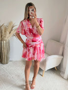 Robe courte rose imprimée Calista avec décolleté cache-cœur, manches fluides et jupe volantée.