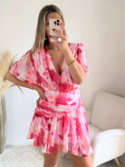 Robe courte rose imprimée Calista avec décolleté cache-cœur, manches fluides et jupe volantée portée par une femme.