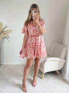 Robe courte corail fleurie Lyséa à manches courtes volantées et taille élastiquée, portée par un mannequin dans un intérieur lumineux.