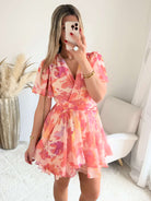 Robe courte rose et pêche imprimée Maëlia avec manches fluides, décolleté cache-cœur et jupe volantée portée par une femme.