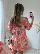 Robe courte rose et pêche imprimée Maëlia avec manches fluides, décolleté cache-cœur et jupe volantée portée par une femme.