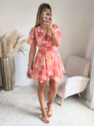 Robe courte rose et pêche imprimée Maëlia avec manches fluides, décolleté cache-cœur et jupe volantée portée par une femme.