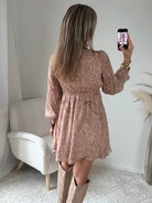 Robe courte Oxane rose poudré à imprimé cachemire, du S au 4XL, avec décolleté cache-cœur et jupe à volants, portée avec des bottes beiges.