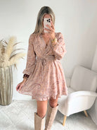 Robe courte Oxane rose poudré à imprimé cachemire, du S au 4XL, avec décolleté cache-cœur et jupe à volants, portée avec des bottes beiges.