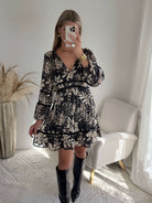 Robe courte noire Bella à imprimé floral écru, manches longues et taille élastiquée.