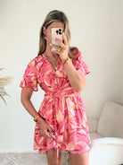 Robe Hany rose corail à imprimé floral, coupe courte fluide avec manches volantées, décolleté croisé et ceinture à nouer à la taille. Disponible du S au 4XL.