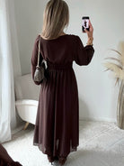 Robe longue fendue Lyana marron, décolleté cache-cœur et manches longues, portée avec des bottes marron.