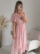 Robe longue rose poudré fleurie Naëlle avec manches fluides et décolleté cache-cœur portée par une femme.