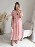 Robe longue rose poudré fleurie Naëlle avec manches fluides et décolleté cache-cœur portée par une femme.