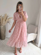 Robe longue rose poudré fleurie Naëlle avec manches fluides et décolleté cache-cœur portée par une femme.