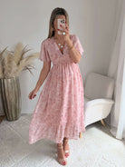 Robe longue rose poudré fleurie Naëlle avec manches fluides et décolleté cache-cœur portée par une femme.