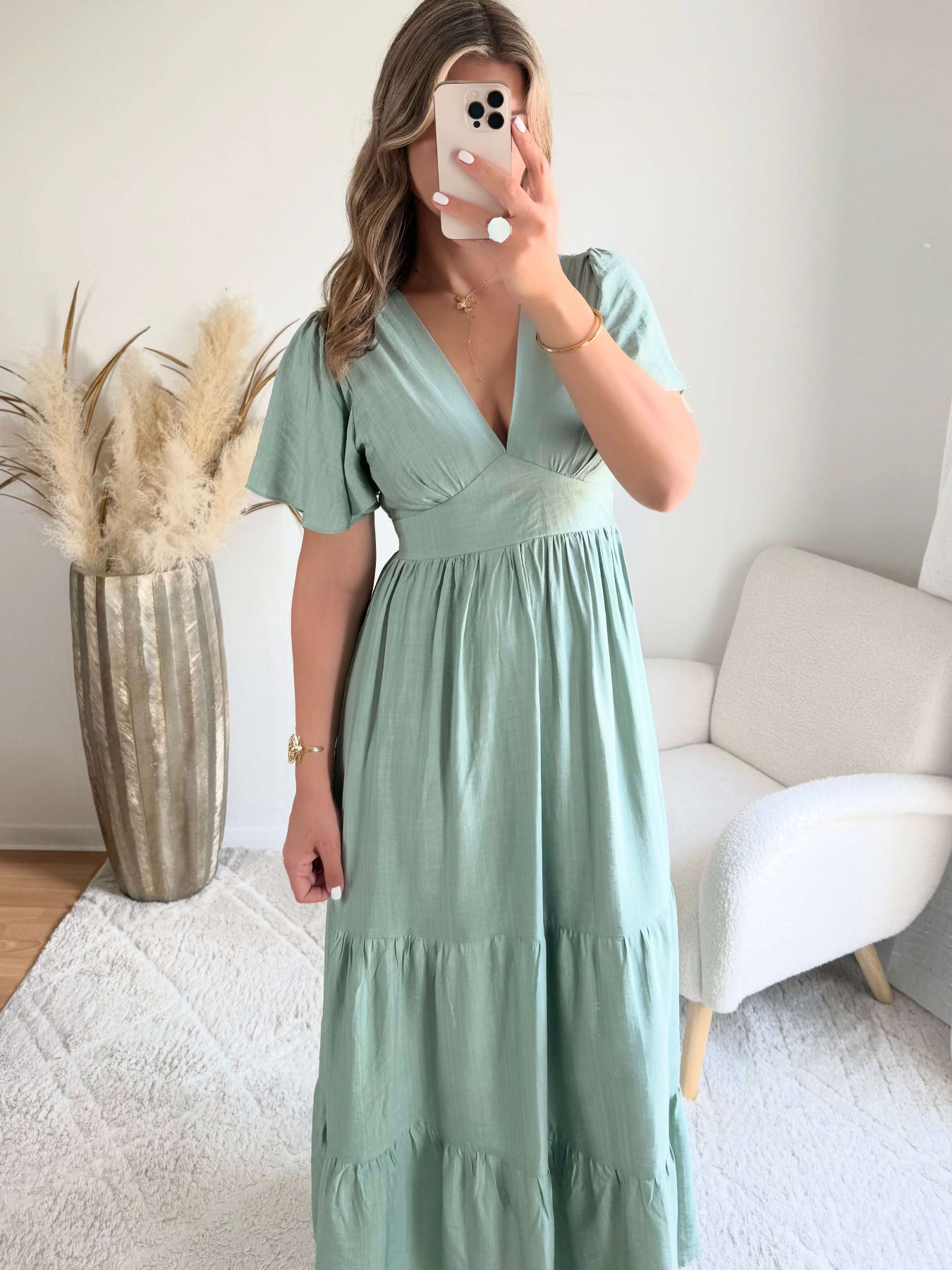 Femme portant une robe longue vert sauge fluide avec manches courtes et décolleté cache-cœur, style bohème chic.