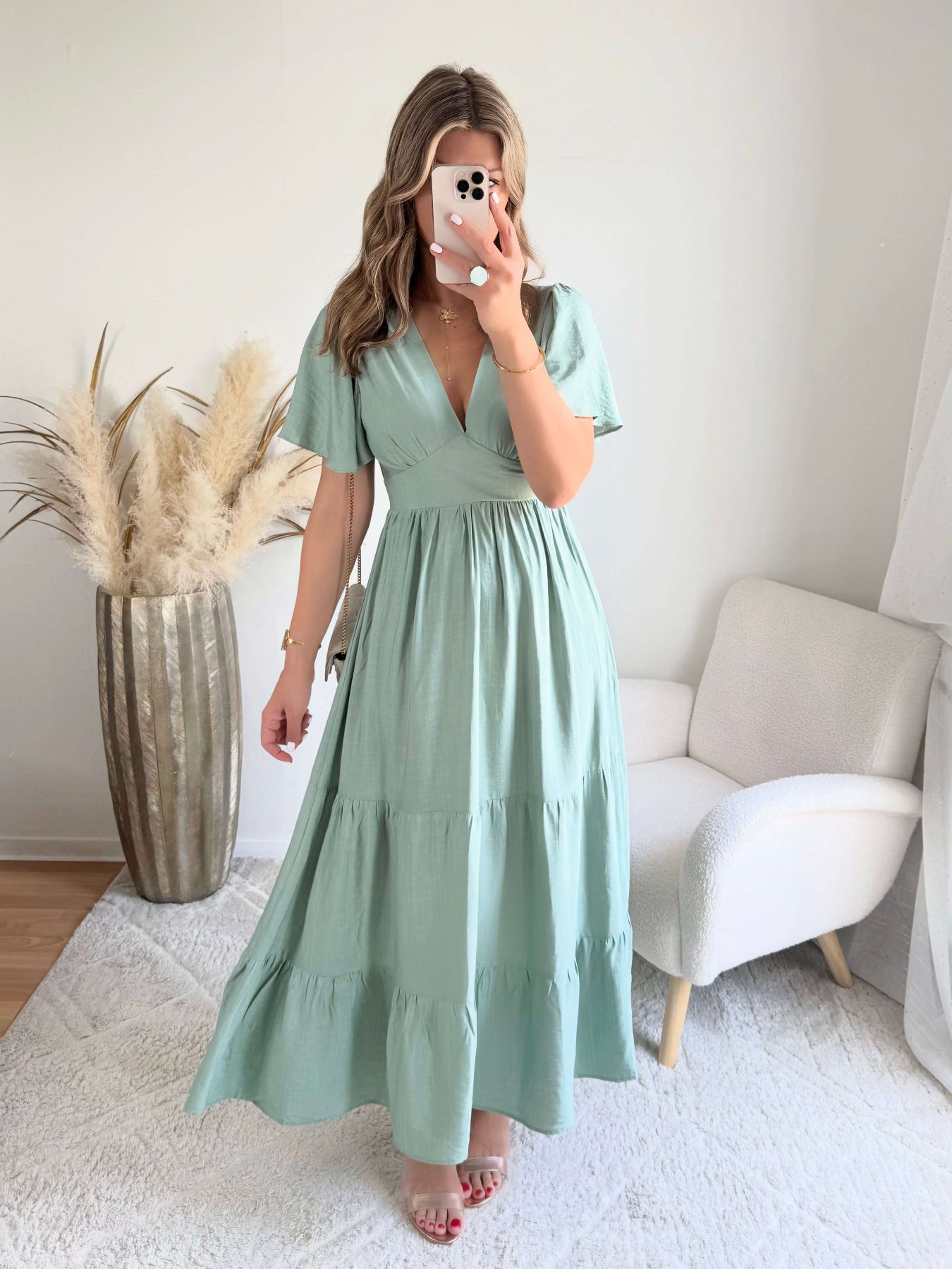 Femme portant une robe longue vert sauge fluide avec manches courtes et décolleté cache-cœur, style bohème chic.