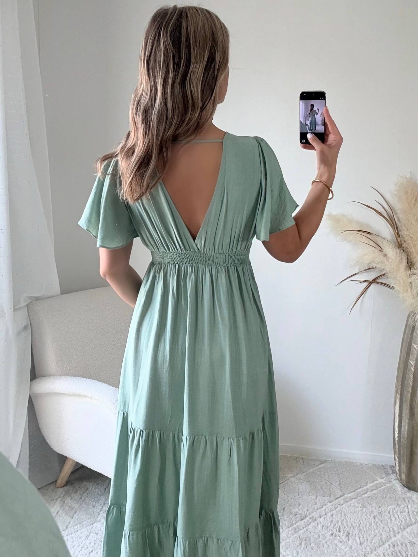 Femme portant une robe longue vert sauge fluide avec manches courtes et décolleté cache-cœur, style bohème chic.