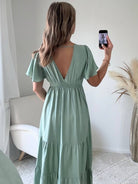 Femme portant une robe longue vert sauge fluide avec manches courtes et décolleté cache-cœur, style bohème chic.
