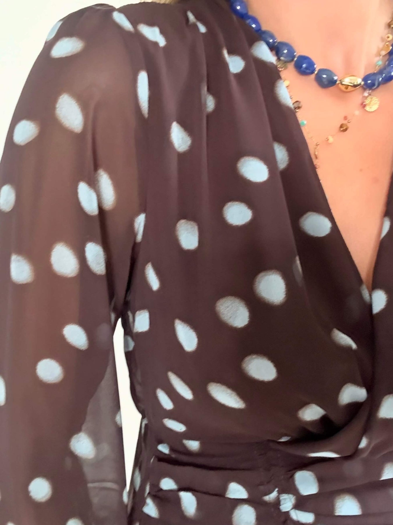 Robe courte marron Nae à pois bleu ciel, du S au L, avec décolleté cache-cœur, manches longues et jupe à volants, portée avec des bottes noires.