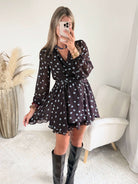 Robe courte marron Nae à pois bleu ciel, du S au L, avec décolleté cache-cœur, manches longues et jupe à volants, portée avec des bottes noires.
