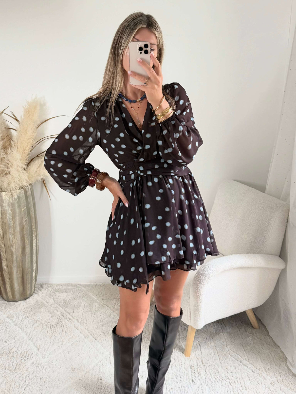 Robe courte marron Nae à pois bleu ciel, du S au L, avec décolleté cache-cœur, manches longues et jupe à volants, portée avec des bottes noires.