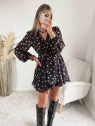 Robe courte marron Nae à pois bleu ciel, du S au L, avec décolleté cache-cœur, manches longues et jupe à volants, portée avec des bottes noires.