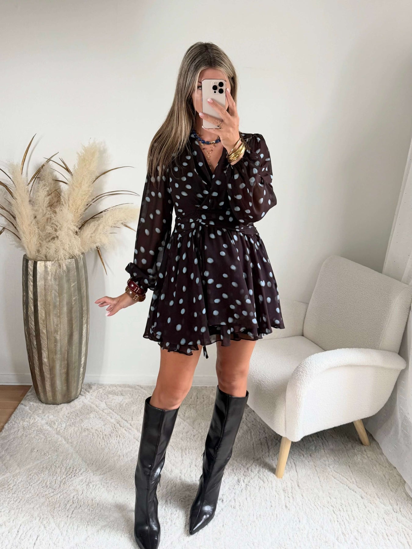 Robe courte marron Nae à pois bleu ciel, du S au L, avec décolleté cache-cœur, manches longues et jupe à volants, portée avec des bottes noires.
