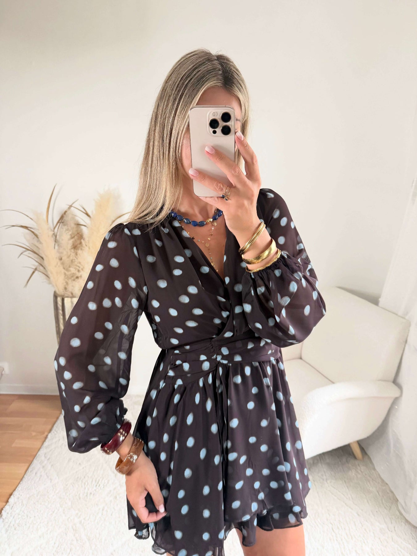 Robe courte marron Nae à pois bleu ciel, du S au L, avec décolleté cache-cœur, manches longues et jupe à volants, portée avec des bottes noires.