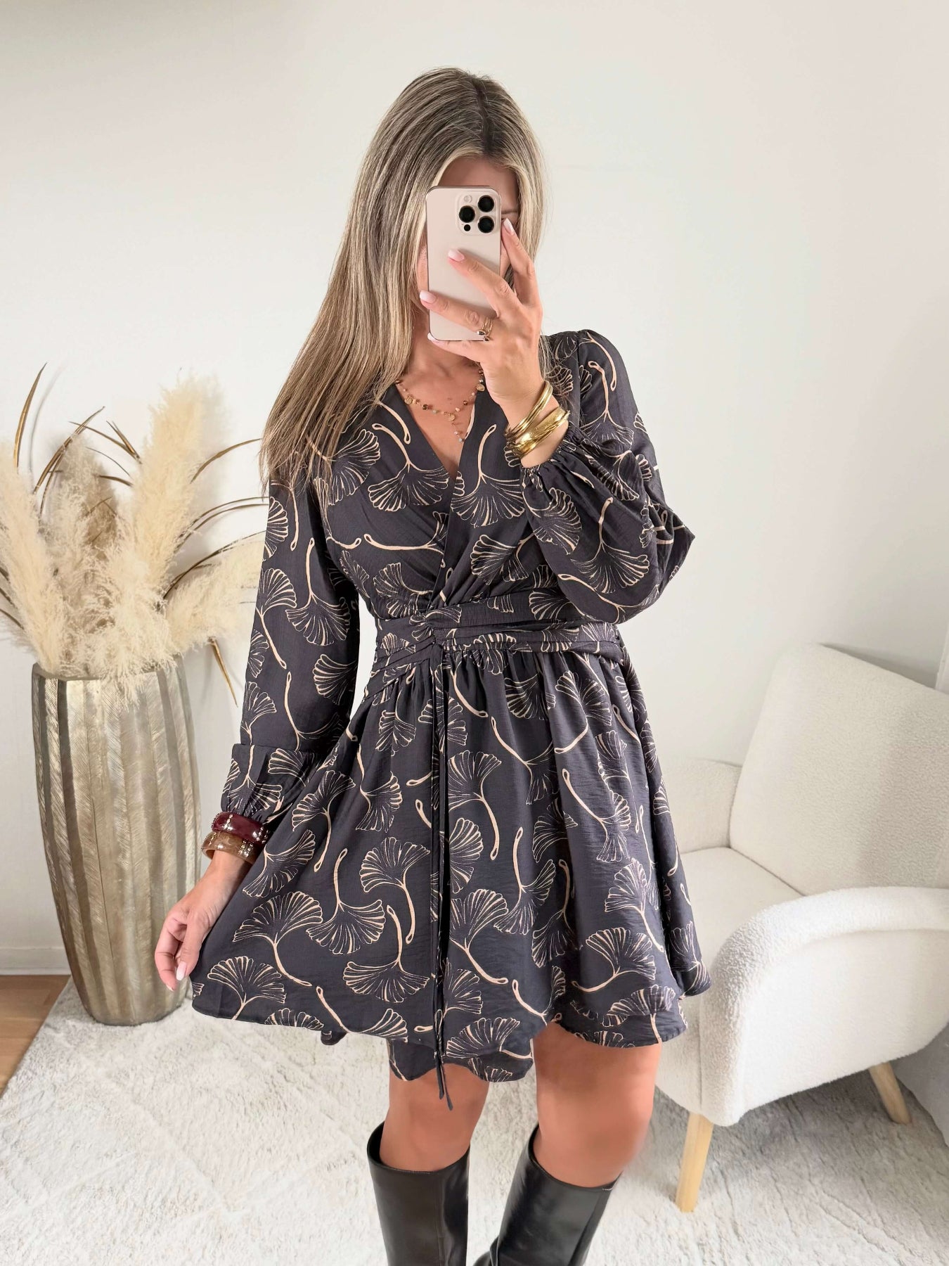 Robe courte noire Zéline du S au 4XL à motifs de feuillage dorés, décolleté croisé en V et manches longues, portée avec des bottes noires.