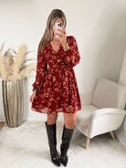 Robe courte terracotta fleurie Gaby, disponible du S au 4XL, à manches longues et décolleté en V, portée avec des bottes noires.