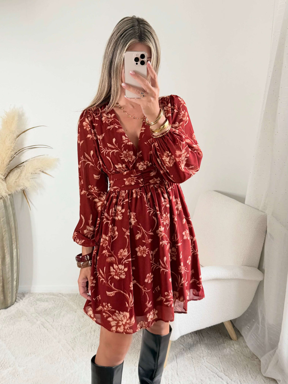 Robe courte terracotta fleurie Gaby, disponible du S au 4XL, à manches longues et décolleté en V, portée avec des bottes noires.