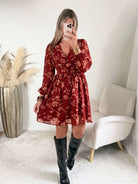 Robe courte terracotta fleurie Gaby, disponible du S au 4XL, à manches longues et décolleté en V, portée avec des bottes noires.