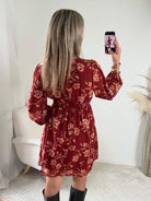 Robe courte terracotta fleurie Gaby, disponible du S au 4XL, à manches longues et décolleté en V, portée avec des bottes noires.