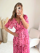 Robe longue plissée rose à imprimé floral avec manches fluides et décolleté croisé.