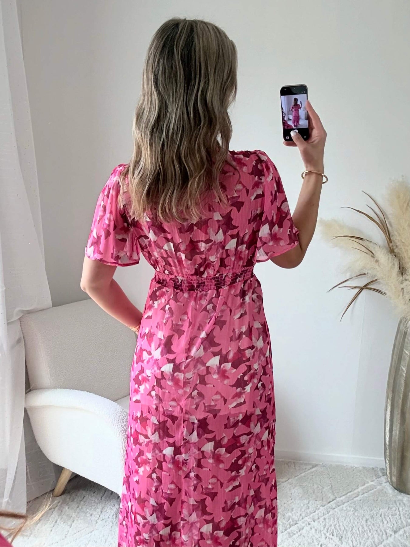 Robe longue plissée rose à imprimé floral avec manches fluides et décolleté croisé.