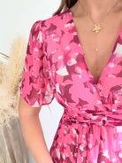 Robe longue plissée rose à imprimé floral avec manches fluides et décolleté croisé.